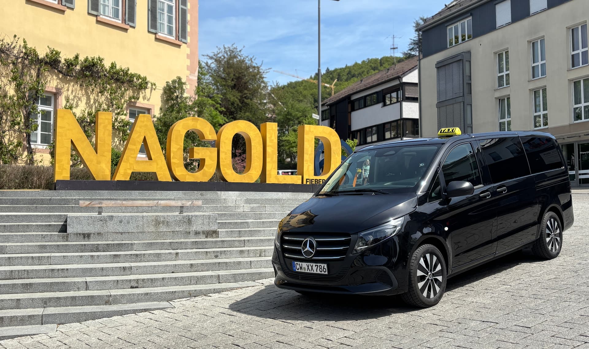 Schwarzes Taxi (Mercedes Vito) von City Taxi Nagold vor dem NAGOLD-Schriftzug